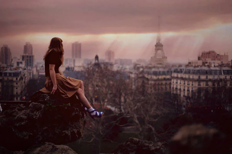 a girl sitting on the edge and looking over Paris